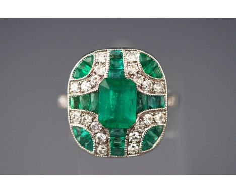 A white metal dress ring. Having a central rectangular cut emerald of approximately 1.60cts. Further set with graduated calib