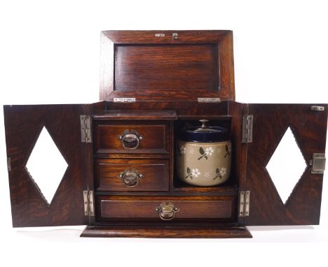 An oak smoker's cabinet with two lozenge glazed doors and lifting top, opening to reveal a fitted interior with pipe rack, tw