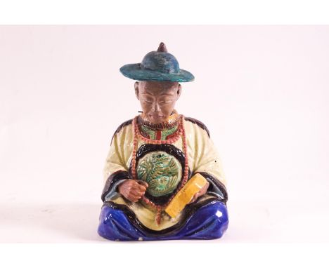 An earthenware figure of a seated Chinese gentleman, wearing a yellow robe with a central dragon motif, playing a drum, with 
