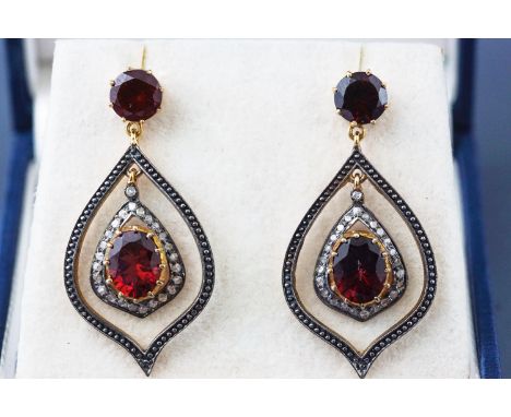 A yellow and white metal pair of drop earrings. Each set with garnets and single cut diamonds. Post and scroll fitting. Stamp