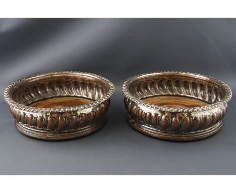 A pair of Sheffield plated decanter coasters with gadrooned edges over a similarly decorated bellied body on turned wood base