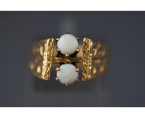 A yellow metal two stone ring set with round cabochon cut commercial opals. Engraved shoulders Size: K 1/2 Hallmarked 9ct gol