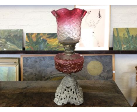 An oil filled lamp with a ruby glass centre and shade with a cast iron pierced base.
