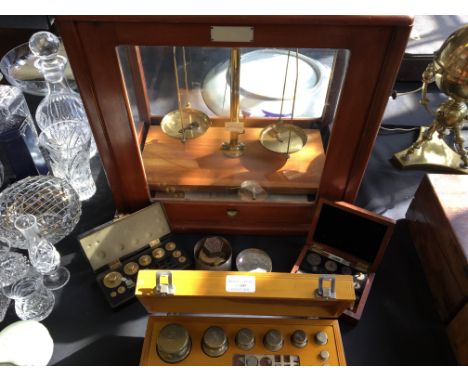 A weighing scale in glass box together with a selection of weights in various boxes.