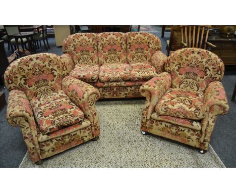 An early-20th century three-piece suite consisting of a two-seater sofa and two conforming armchairs, upholstered in cream wi