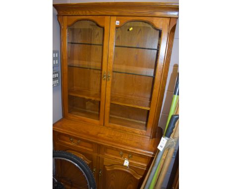 A modern elm dresser, glazed panel doors open to reveal glass and single wooden shelf above two short drawers and cupboard do