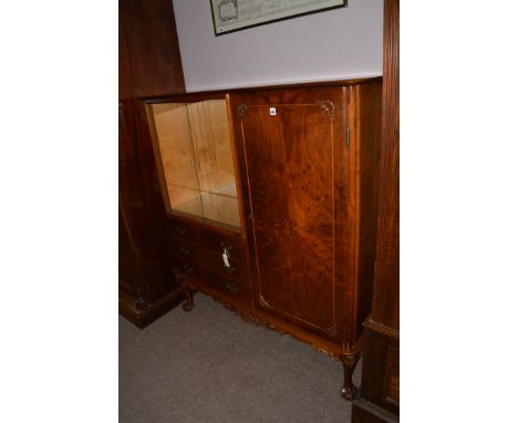 A 20th Century walnut veneered drinks cabinet with glazed panel sliding doors above three drawers and cupboard door to right 