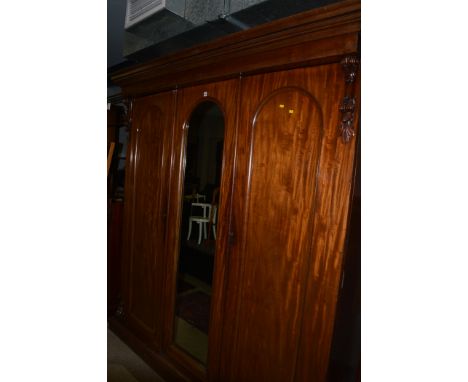 A Victorian mahogany two door wardrobe the central mirror panel door flanked by arched panel doors opening to reveal hanging 