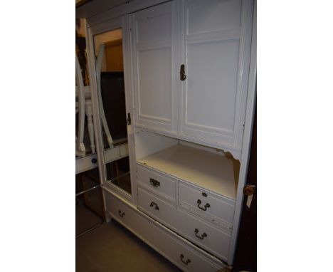 A Victorian white painted wardrobe, the mirrored door opening to reveal hanging space, a pair of cupboard doors above open sh