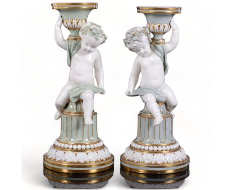 A pair of Minton's green and gilded white porcelain cherub candlesticks holding an urn, H23.5cm1 cherub has had their left le