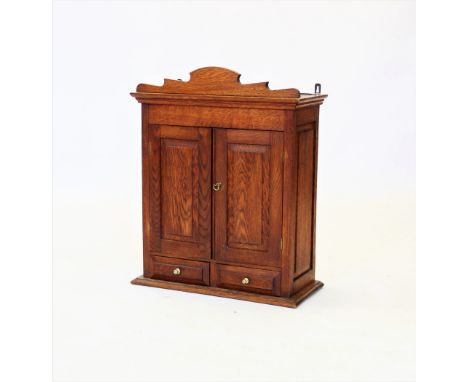 An early 20th century oak wall cabinet, with a shaped pediment above a pair of panelled doors, enclosing a single shelf, over