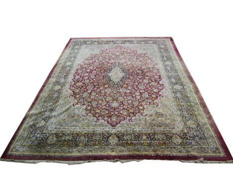 A large Kirman carpet, the central floral medallion surrounded by foliate scrolls, on red ground, signed to one end, 495 x 36