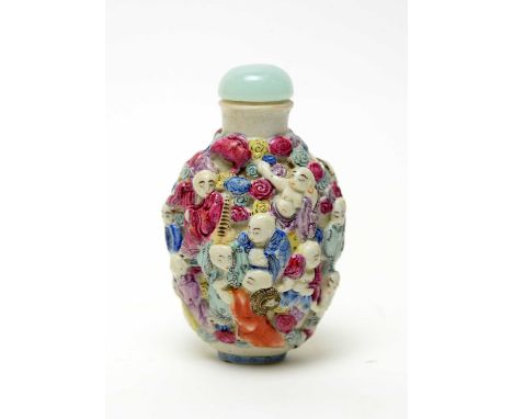 A Chinese famille rose porcelain snuff bottle, moulded in relief and picked out in colours with deities, pale green bowenite 