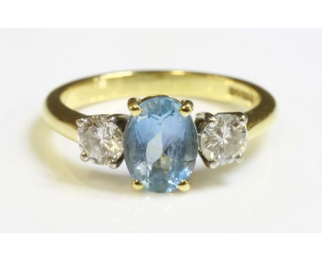 An 18ct gold aquamarine and diamond three stone ring,with an oval mixed cut aquamarine four claw set to a yellow collet.  A b