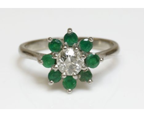 A white gold, diamond and emerald cluster ring,with an old European cut diamond, claw set to the centre.  A surround of eight