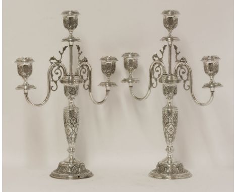 A pair of Persian metalwares three light candelabra,the baluster stems on domed circular feet, all over engraved with arabesq