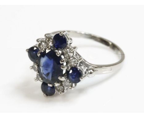 An 18ct white gold, sapphire and diamond cluster ring, with an oval mixed cut sapphire claw set to the centre.  A circular mi