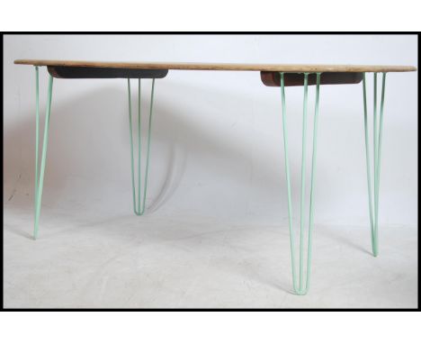 An upcycled retro 20th century Ercol elm wood dining table being raised on green painted hairpin metal legs.