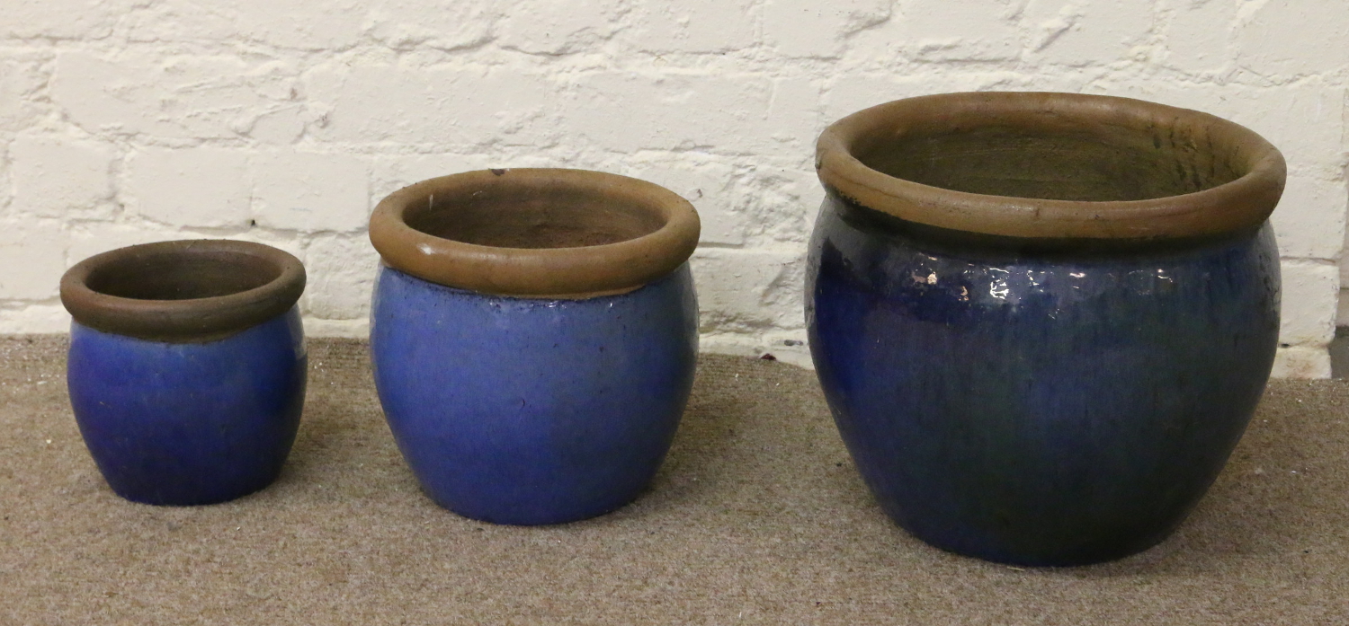 Three graduated blue glazed terracotta plant pots.