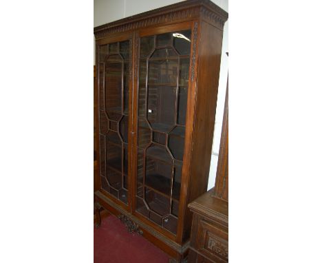 A large 19th century mahogany double door glazed bookcase on stand, having a Gothic arch frieze and applied floral carvings 