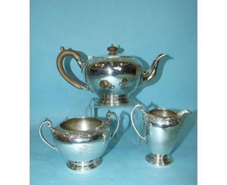 A three-piece tea service comprising a bullet-shaped teapot, cream jug and sugar basin, with engraved floral and leaf rim and