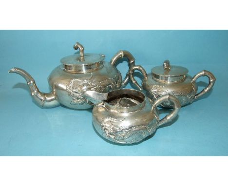 A three-piece Chinese silver tea service of compressed circular shape, decorated with a dragon and having bamboo spout and ha