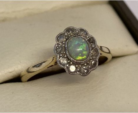 An 18ct gold and platinum diamond and opal dress ring. Central oval opal surrounded by 10 small round cut diamonds. Inside ba