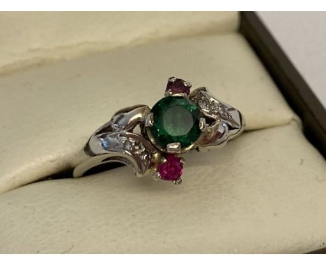 A 14ct white gold dress ring set with emerald ruby and diamond stones. Central round cut emerald with a small ruby and 2 smal