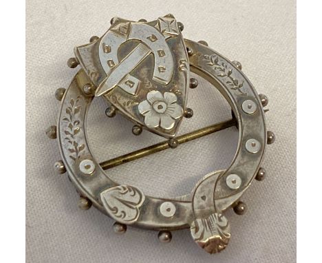 A vintage silver circular shaped sweetheart brooch with shield, horseshoe and dagger detail. Worn silver marks to reverse. We