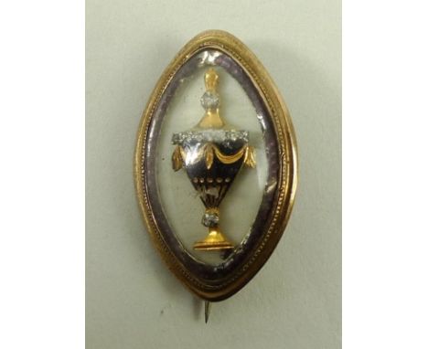 A George III gold, enamel and diamond set mourning brooch of ovoid form set with an urn against a white ground within a borde