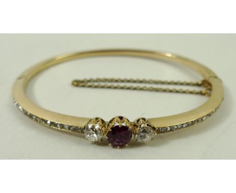 An 18ct gold, ruby and diamond three stone set bangle flanked by pave set diamonds, on a snap clasp with safety chain, as fit