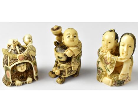 Three Japanese netsuke comprising a man holding up a mask, a child riding a cat and a child hiding under a basket with anothe