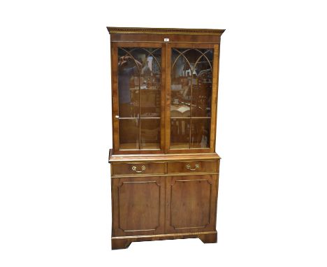 A reproduction yew wood bookcase with dentil moulded cornice above pair of glazed doors enclosing two adjustable shelves, abo