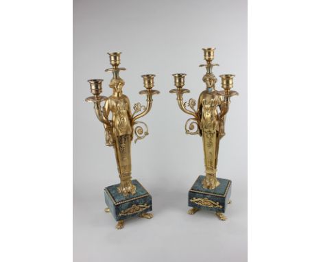 A pair of Regency style gilt metal three-light candelabra with female figure holding aloft branches, on green marble plinth a