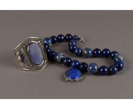 A modern associated suite of lapis lazuli jewellery, including a large white metal cuff bangle, a large bead necklace, a broo