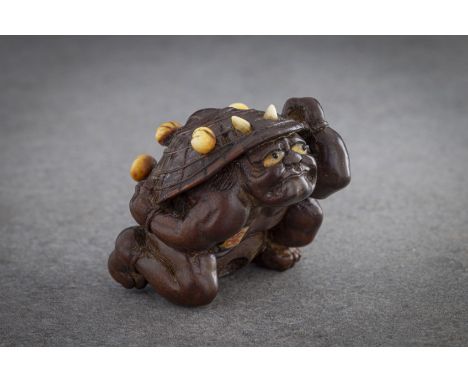 A WOOD NETSUKE OF A COWERING ONI Unsigned, Japan, Nagoya, 19th century, Edo period (1615-1868) The oni cowering underneath a 