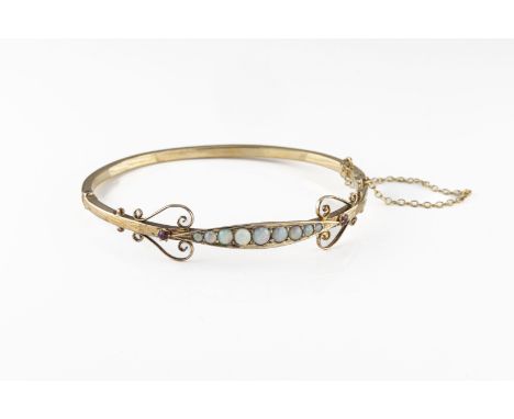 An early 20th century yellow gold opal and ruby hinged bangle, set with nine graduated round cabochon opals, flanked by two r