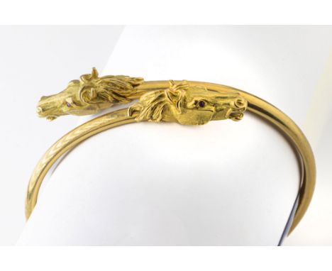 An 18ct yellow gold bangle the terminals cast as horses heads, having ruby set eyes, maker's mark 'S&amp;S', London import ma