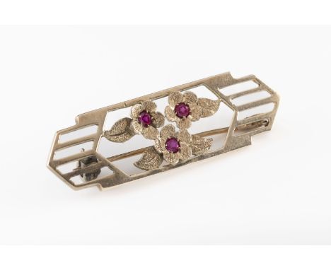 A 9ct yellow gold and ruby Art Deco brooch with three cast central flowers, set with round cut rubies, within geometric borde