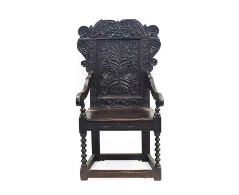 A 17th Century Joined Oak Wainscot Armchair, the scrolled and vine carved top rail above a fielded back support with stylised