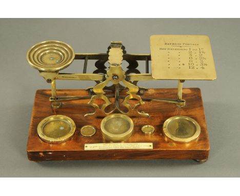 A set of Victorian brass postal scales, marked with rates of postage to the scale and complete with weights, oak base.  Width