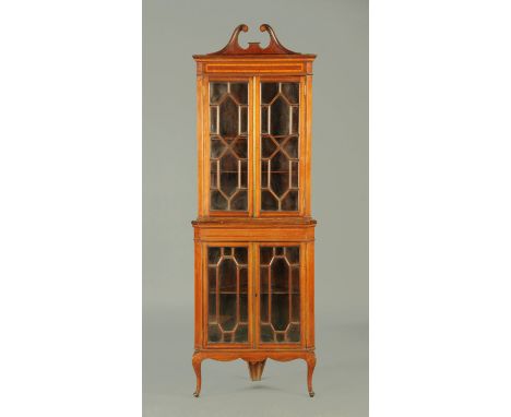 An Edwardian inlaid mahogany standing corner cupboard, with swans neck pediment above a pair of glazed doors enclosing shelve