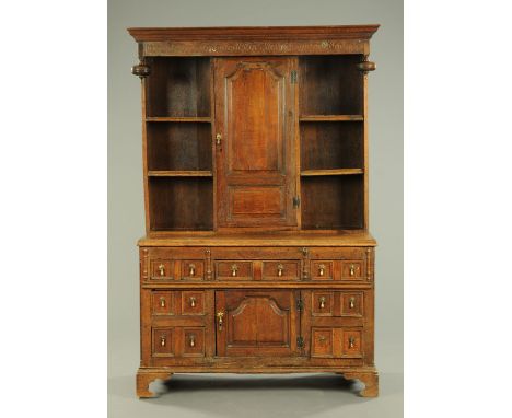 An antique oak dresser, with moulded cornice, carved frieze and long centre cupboard door flanked on either side by shelves, 