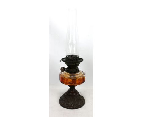 A late Victorian oil lamp with amber tinted reservoir and embossed metal base, height excluding chimney 27cm.