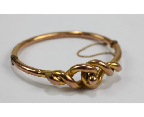 A 9ct yellow gold hollow snap bangle decorated with ornamental knot motif, with safety chain, aperture 6 x 5cm, approx 9.1g. 
