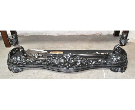 A cast iron fender of serpentine outline, and a set of three 19th century polished steel fire tools.