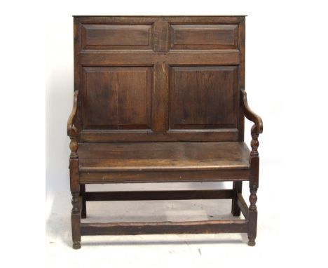 An oak settle of small proportions with panel back, swept arms, plank seat and turned and block legs united by stretchers.