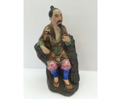 A Chinese Republic ceramic figure modelled as a wood gatherer seated holding a cigar dressed in traditional costume, possibly