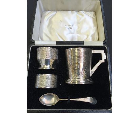 A cased Art Deco silver Christening set with engine turned decoration, comprising mug, egg cup, serviette ring and spoon.