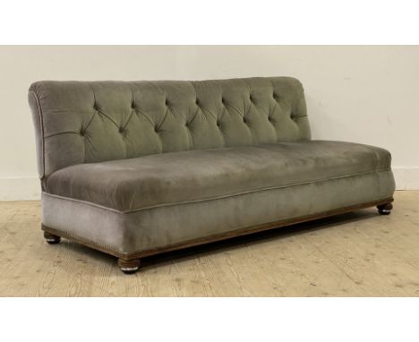 A late Victorian upholstered banquet or bench sofa, covered in deep buttoned green velvet, raised on compressed bun supports 
